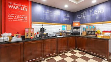 Una zona de cocina con una estación de gofres, una cafetera y diversos electrodomésticos.