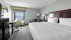 Quarto de hotel com uma cama grande, uma escrivaninha com cadeira, uma mesinha de centro com abajures e uma janela com vista.