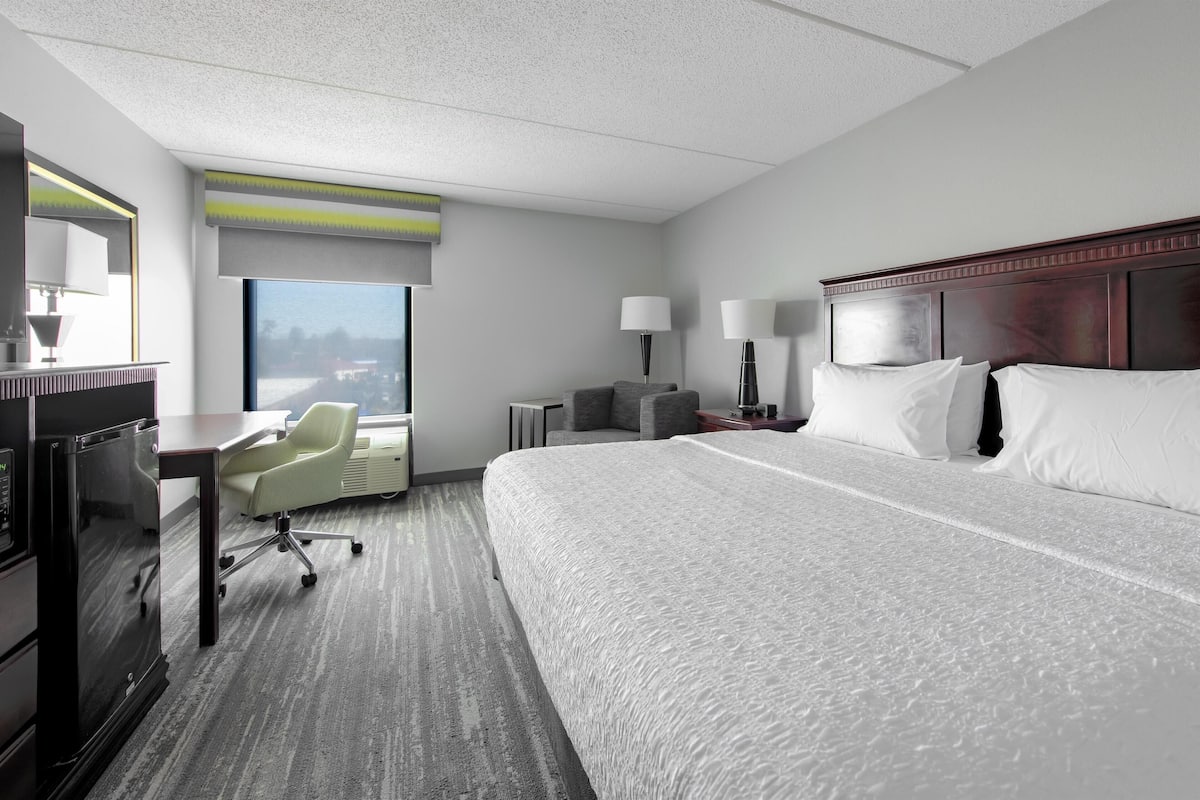 Une chambre d’hôtel avec un grand lit, un bureau avec une chaise, une petite table avec des lampes et une fenêtre donnant sur un beau paysage.