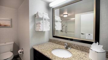 A bathroom with a granite countertop sink, a large mirror, and a towel rack with folded towels.