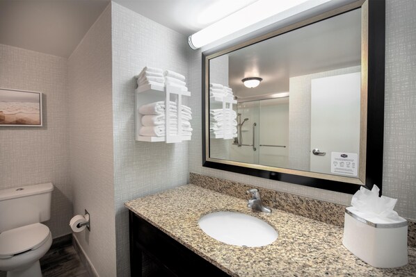 Une salle de bain avec un lavabo doté d’un plan de travail en granit, un grand miroir et un porte-serviettes avec des serviettes pliées.