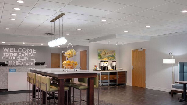 A hotel lobby with a reception desk, seating area, and a kitchen in the background. - Hampton Inn Tallahassee-Central (Tallahassee)