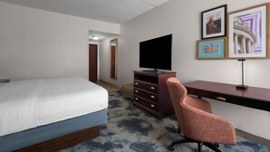 A hotel room with a bed, a desk, a chair, a television, and framed pictures on the wall.
