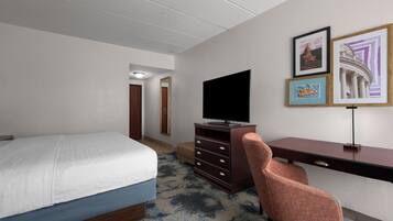 Habitación de hotel con cama, escritorio, silla, televisor y cuadros en la pared.
