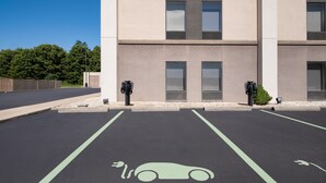 A parking lot with electric vehicle charging stations, a building with a brick facade, and a clear blue sky.