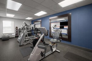 Un gimnasio con equipo de ejercicio diverso, un espejo grande y un lema motivacional.