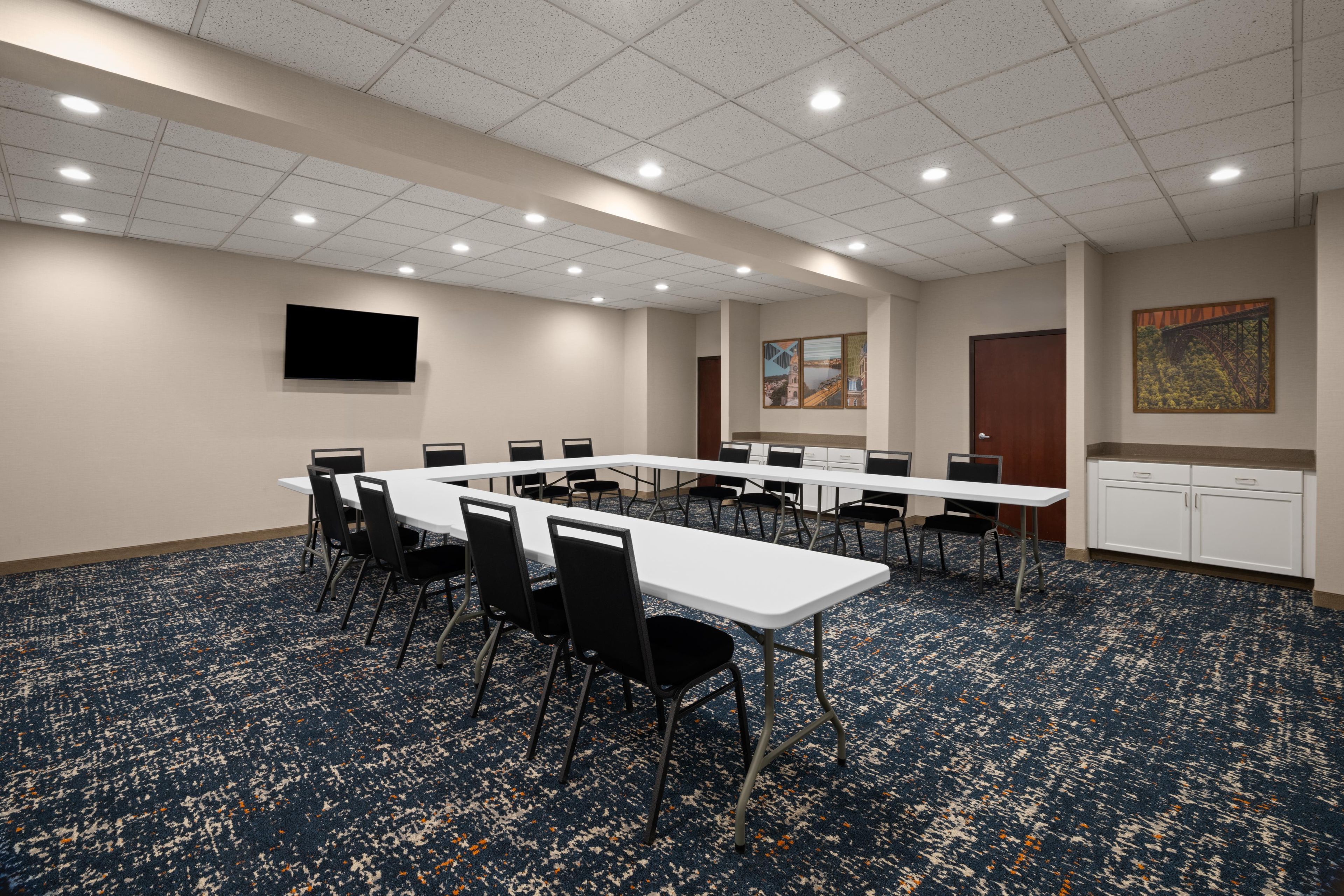 A conference room with a long table, chairs, a flat-screen TV, artwork on the wall, and a carpeted floor.