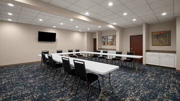 A conference room with a long table, chairs, a flat-screen TV, artwork on the wall, and a carpeted floor.