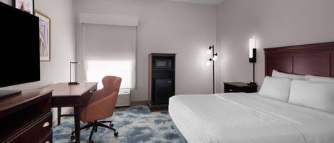 A hotel room with a bed, desk, chair, TV, microwave, and lamp.