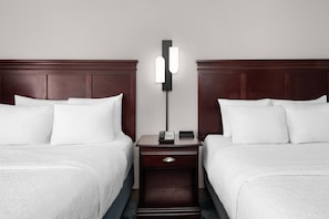 A hotel room with two single beds, a nightstand with a phone and a lamp, and a plain wall. - Hampton Inn Winfield/teays Valley (Hurricane)
