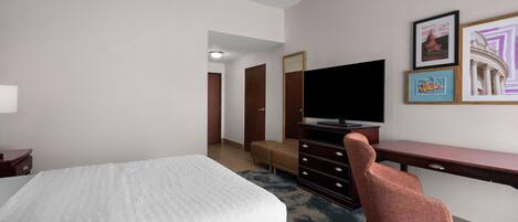 A hotel room with a bed, a desk, a chair, a television, and framed pictures on the wall.