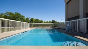 A swimming pool with a white fence, clear blue water, and a building in the background. - Hampton Inn Winfield/teays Valley (Hurricane)