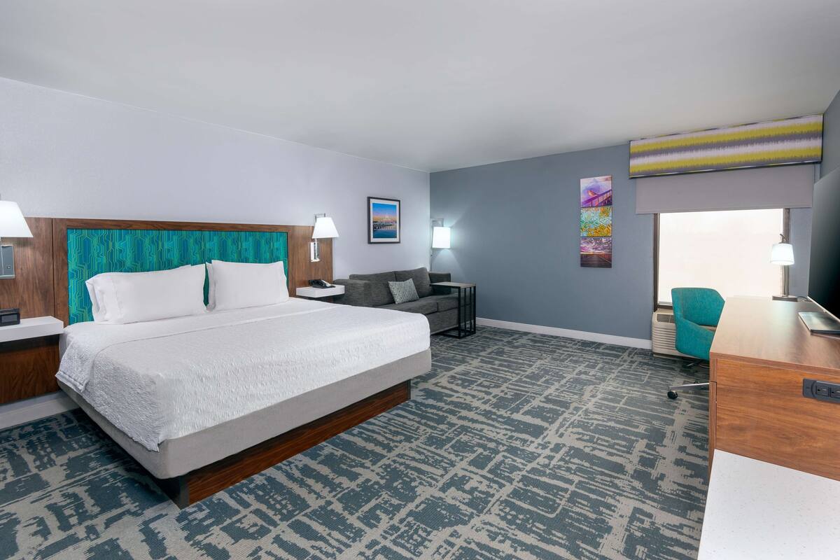 A hotel room with a large bed, a desk, a sofa, and a chair.