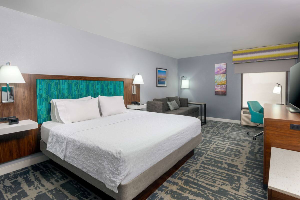A hotel room with a large bed, a sofa, a desk, and a television.