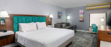 A hotel room with a large bed, a sofa, a desk, and a television.