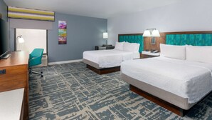 A hotel room with two beds, a desk, a chair, and a large window.
