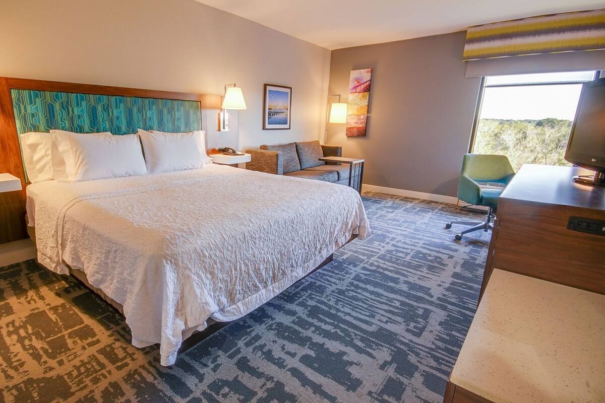 A hotel room with a large bed, bedside lamps, a desk, a chair, and artwork on the walls.
