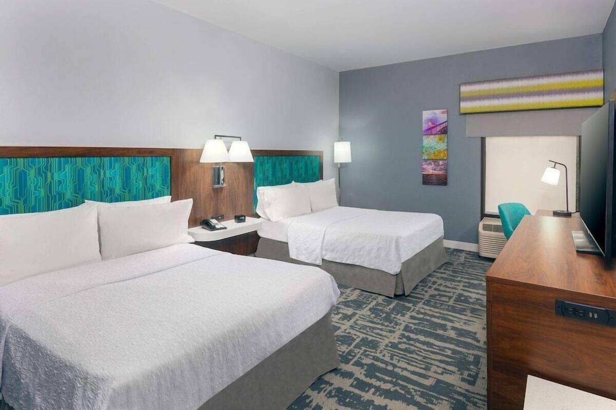 A hotel room with two beds, a desk, a television, and a patterned carpet.