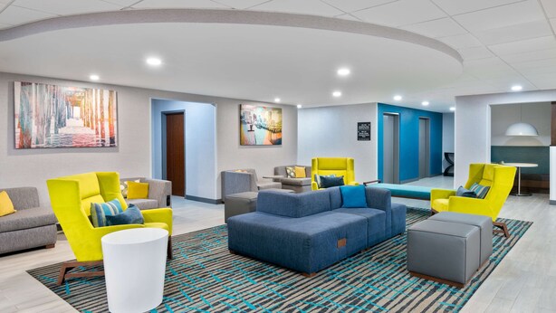 A modern lobby with a blue sofa, yellow armchairs, a white coffee table, and a patterned rug.