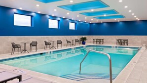 A pool area with lounge chairs and tables, a tiled pool, and blue walls with windows.