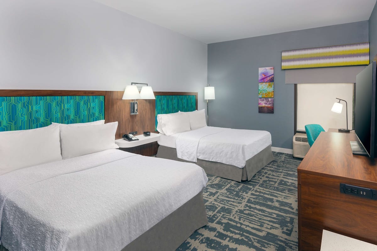 A hotel room with two beds, a desk, a TV, a phone, and a painting on the wall.