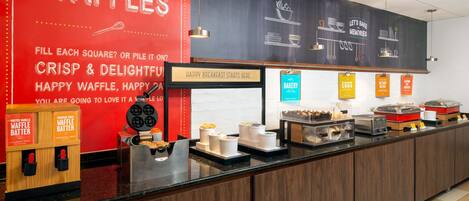 A breakfast bar with waffle stations and bakery items.