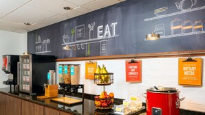 A breakfast bar with a chalkboard wall displaying the word "EAT" and various food-related drawings. There are signs indicating dietary needs and caution for hot surfaces.