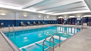 Ein Swimmingpool mit Liegestühlen, einer gefliesten Wand und Blick durch Glastüren.