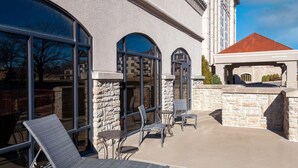Eine Terrasse im Freien mit Lounge-Möbeln, Tischen, Steinmauern und großen Fenstern.