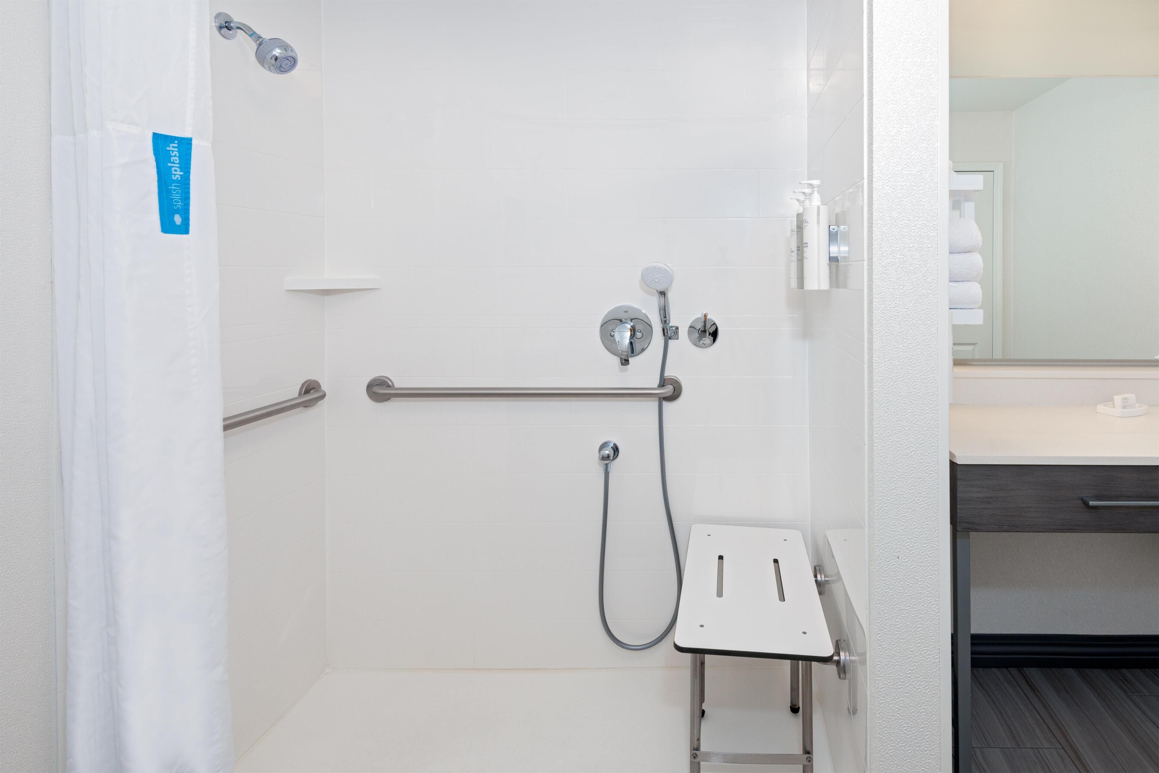 A shower with a handheld showerhead, a handheld faucet, and a grab bar.