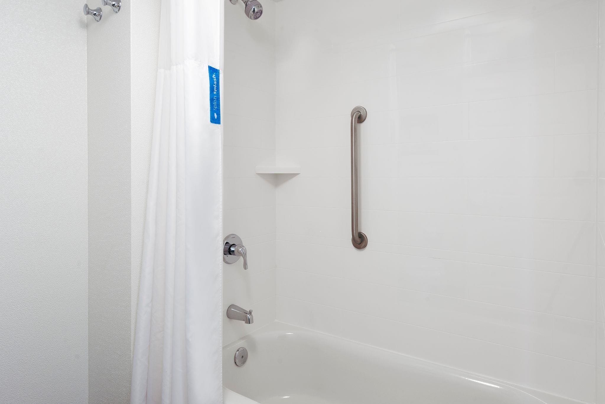 Un baño con una bañera blanca, una ducha con barra de apoyo y una pared blanca con un letrero azul.