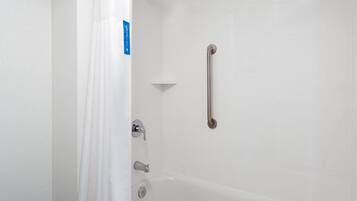 A bathroom with a white bathtub, a shower with a grab bar, and a white wall with a blue sign.