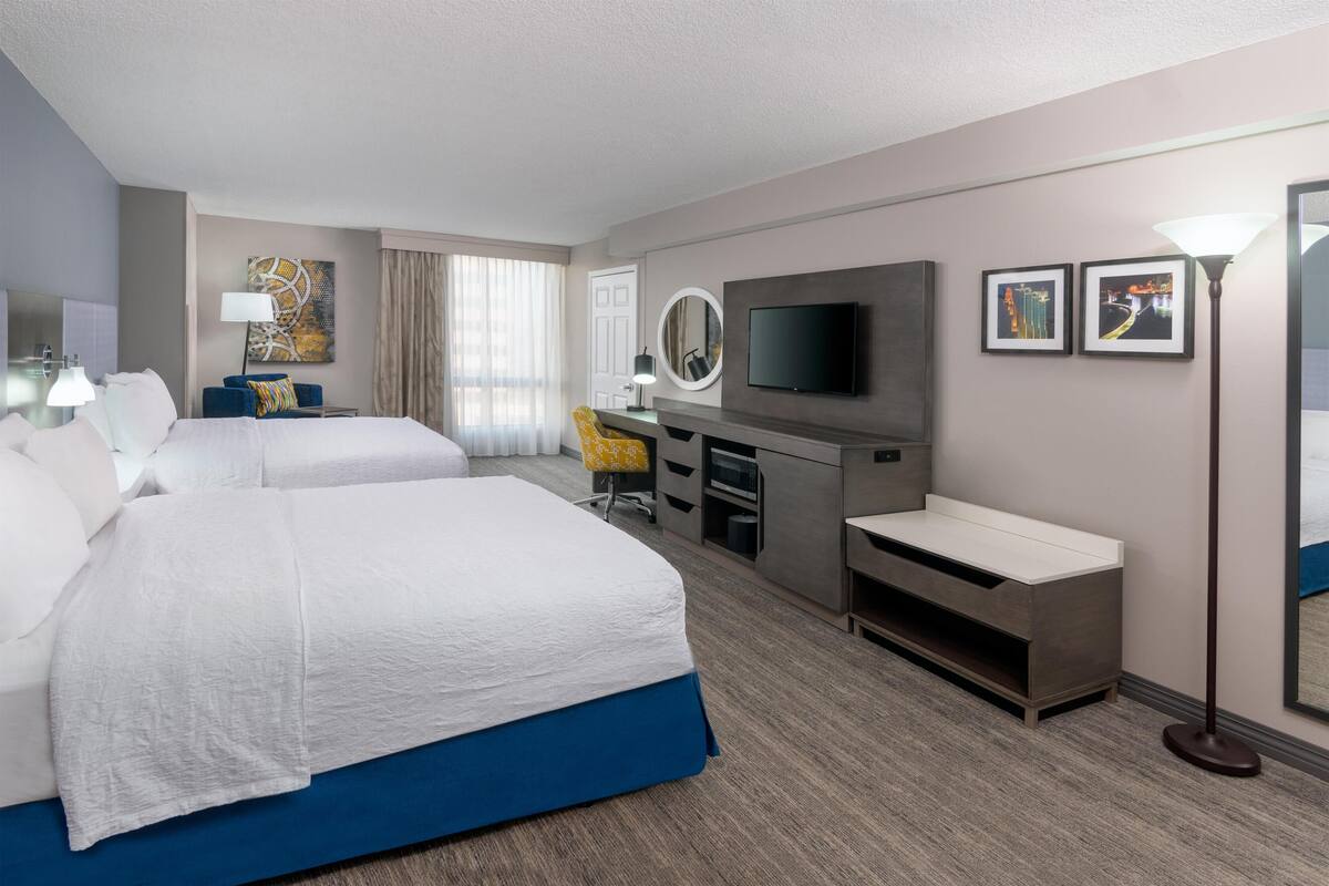 Une chambre d’hôtel avec deux lits, un bureau, une télévision et une grande fenêtre.