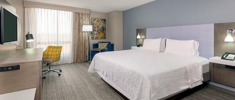 A hotel room with a bed, desk, chair, and a TV.