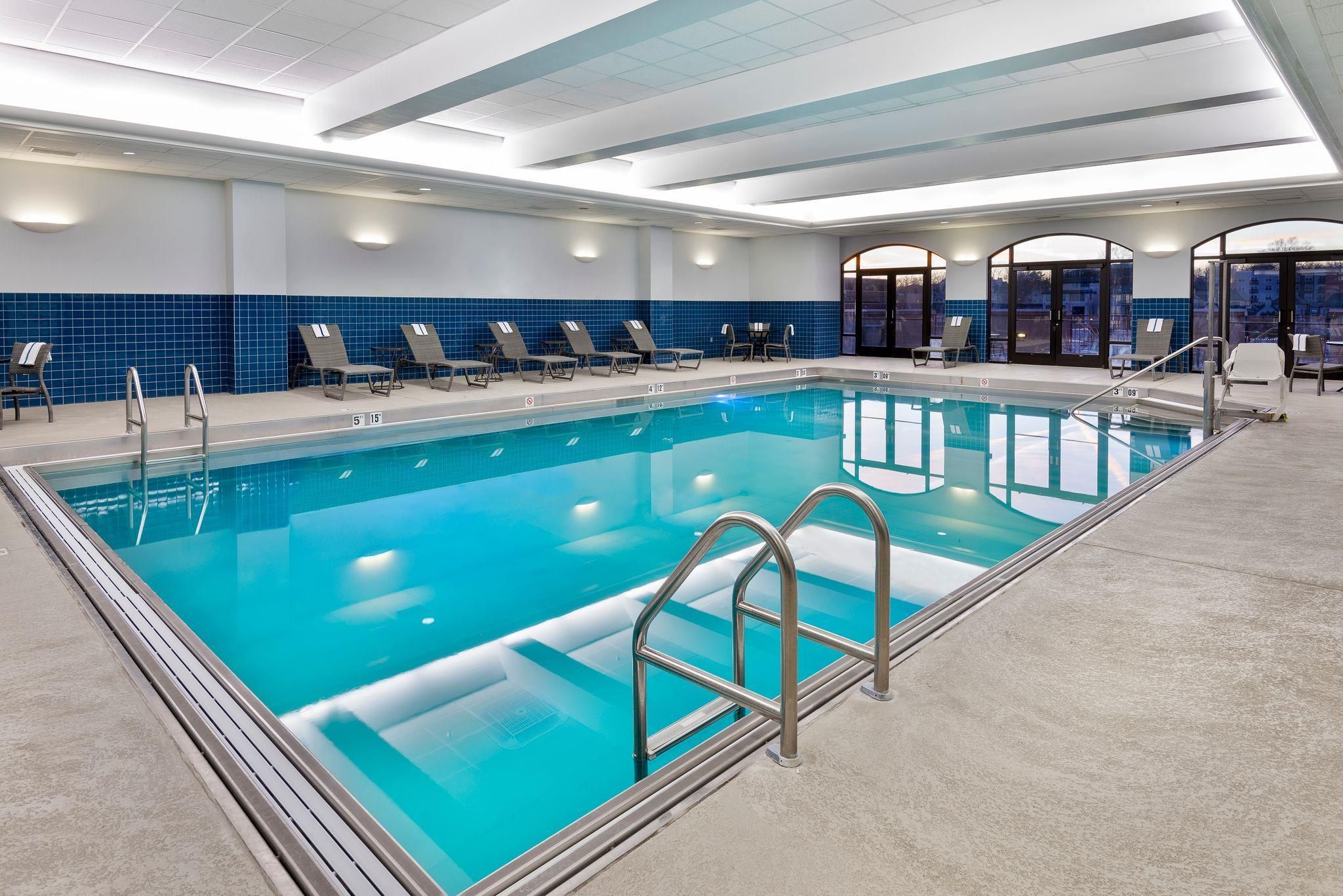 A swimming pool with lounge chairs, a tiled wall, and a view through glass doors.