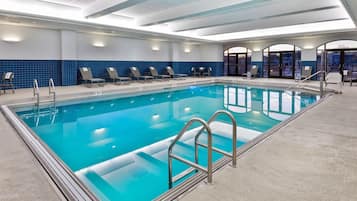 A swimming pool with lounge chairs, a tiled wall, and a view through glass doors.