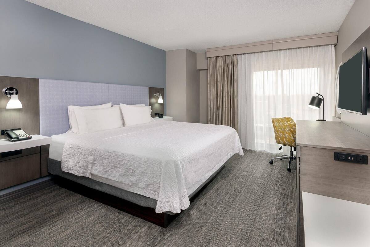 Une chambre d’hôtel comprenant un lit, des tables de chevet, un bureau avec une chaise, une télévision et des rideaux.