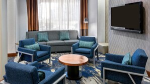Ein modernes Hotelzimmer mit einer Sitzecke, Sesseln, einem Couchtisch und einem an der Wand montierten Flachbildfernseher.