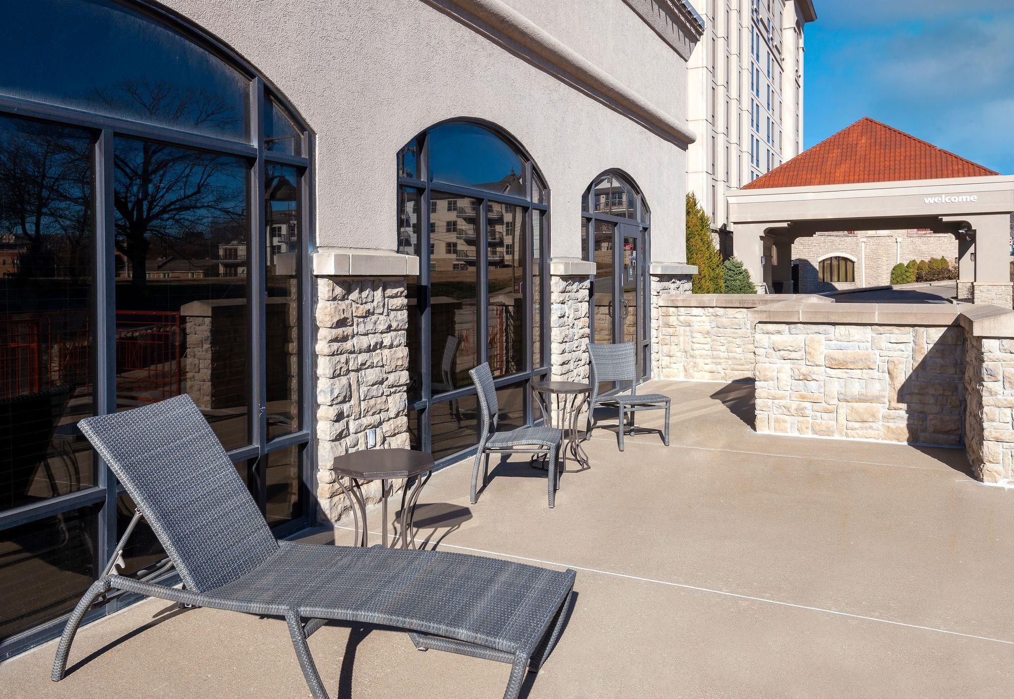 An outdoor patio with lounge chairs and tables, stone walls, and large windows.
