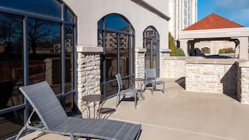 An outdoor patio with lounge chairs and tables, stone walls, and large windows.
