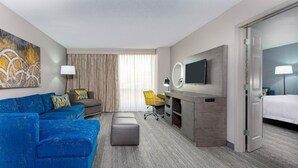 Ein Hotelzimmer mit einem blauen Sofa, einem Schreibtisch mit Stuhl, einem Fernseher und einem Bett.
