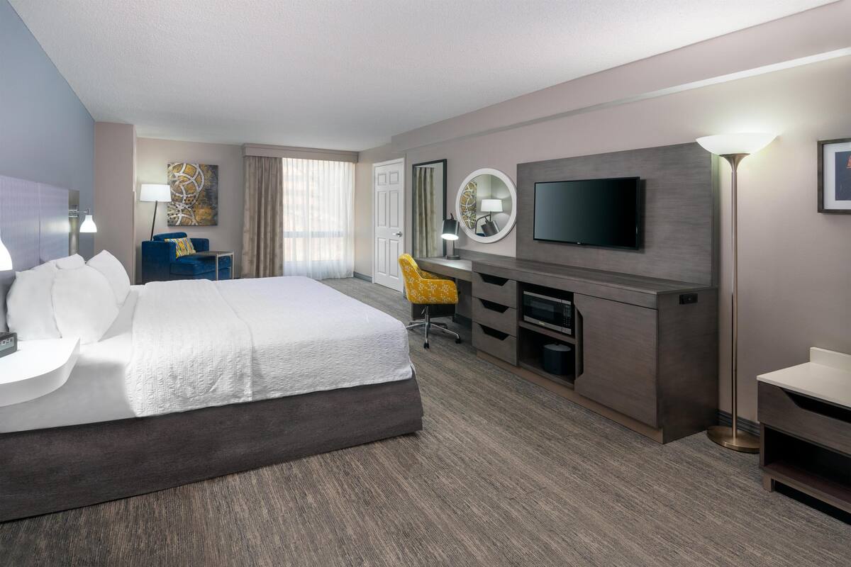 Une chambre d’hôtel avec un grand lit, un bureau avec une chaise, un téléviseur à écran plat et une lampe de bureau.