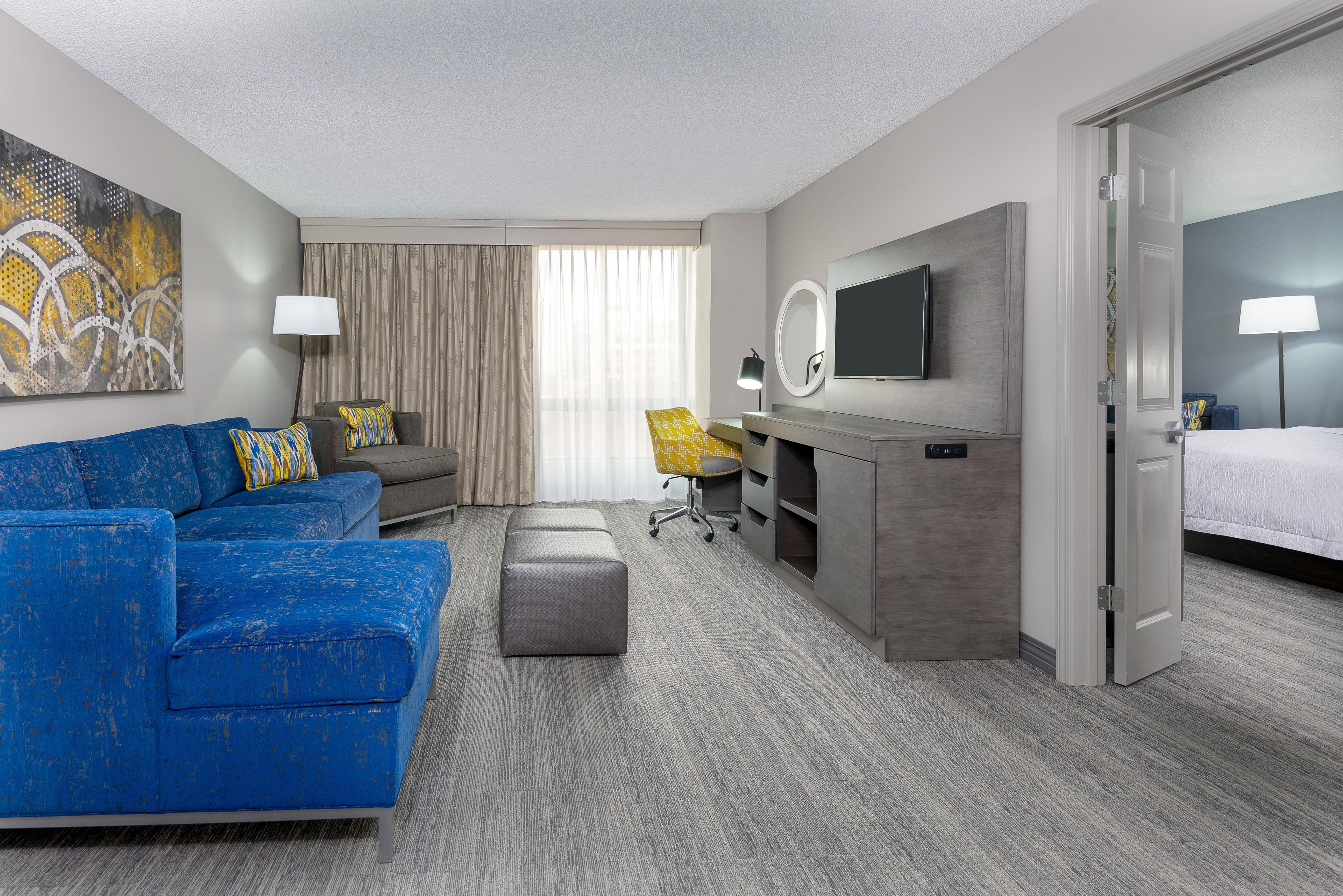 Een hotelkamer met een blauwe bank, een grijze fauteuil, een bureau met een stoel, een televisie en een bed.