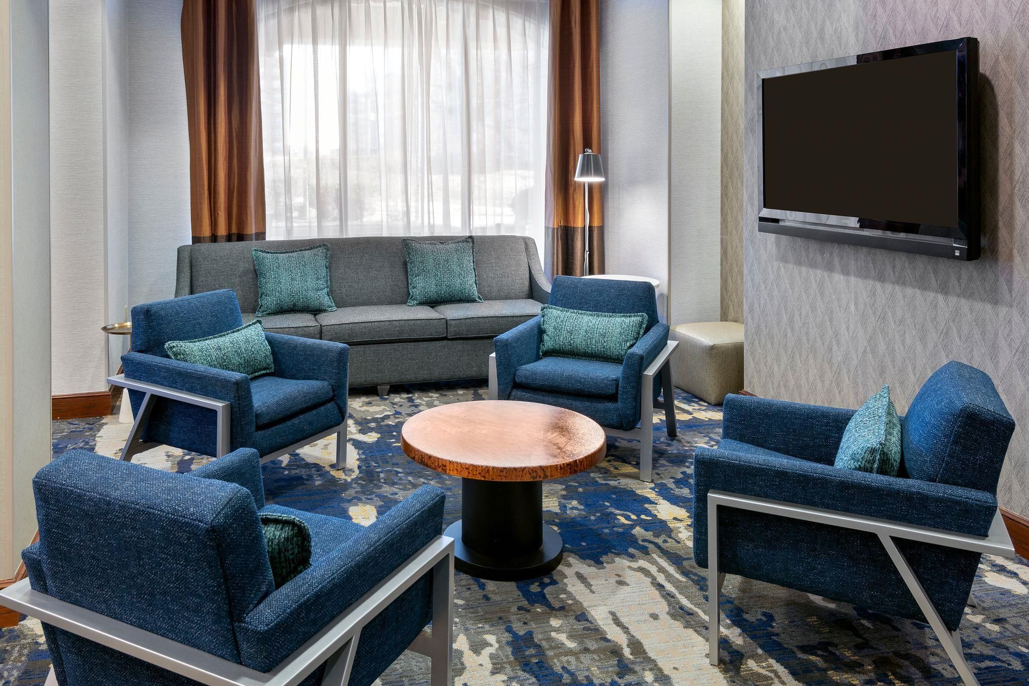 Una habitación de hotel moderna con sofá, sillones, una mesa de centro y un televisor de pantalla plana montado en la pared.
