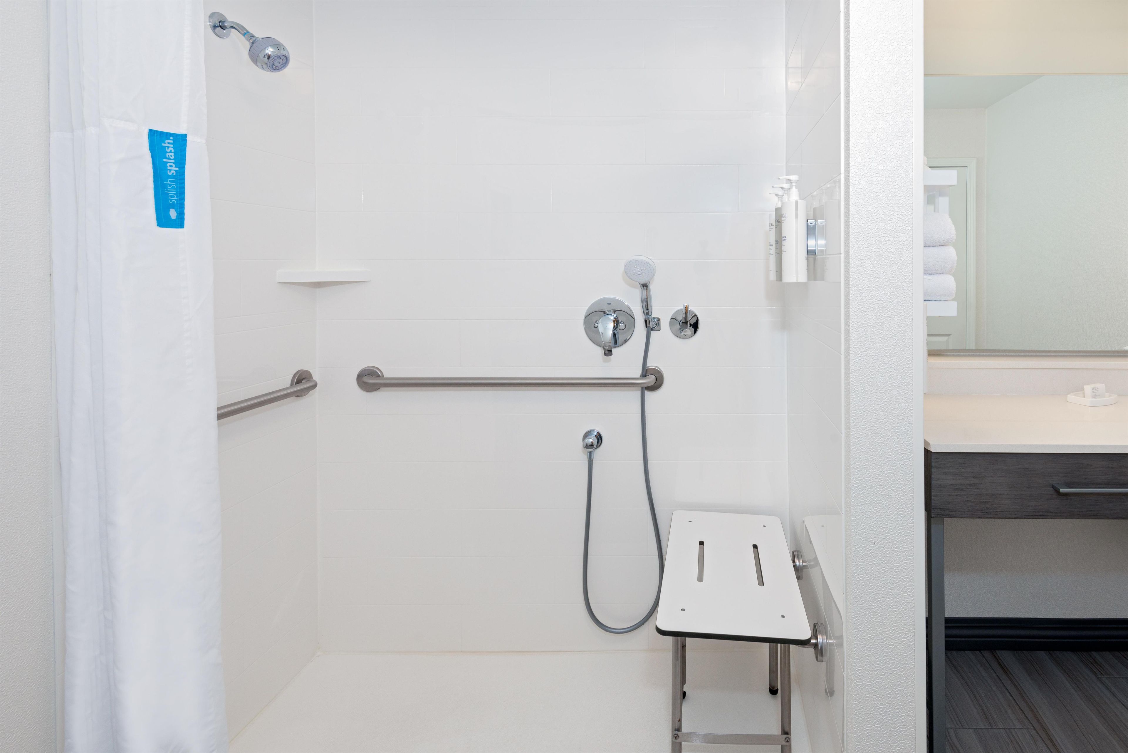 A bathroom with a shower, grab bars, and a towel rack.