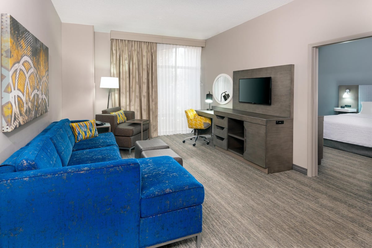 Une chambre d’hôtel avec un canapé bleu, une télévision, un bureau, une chaise et un lit.