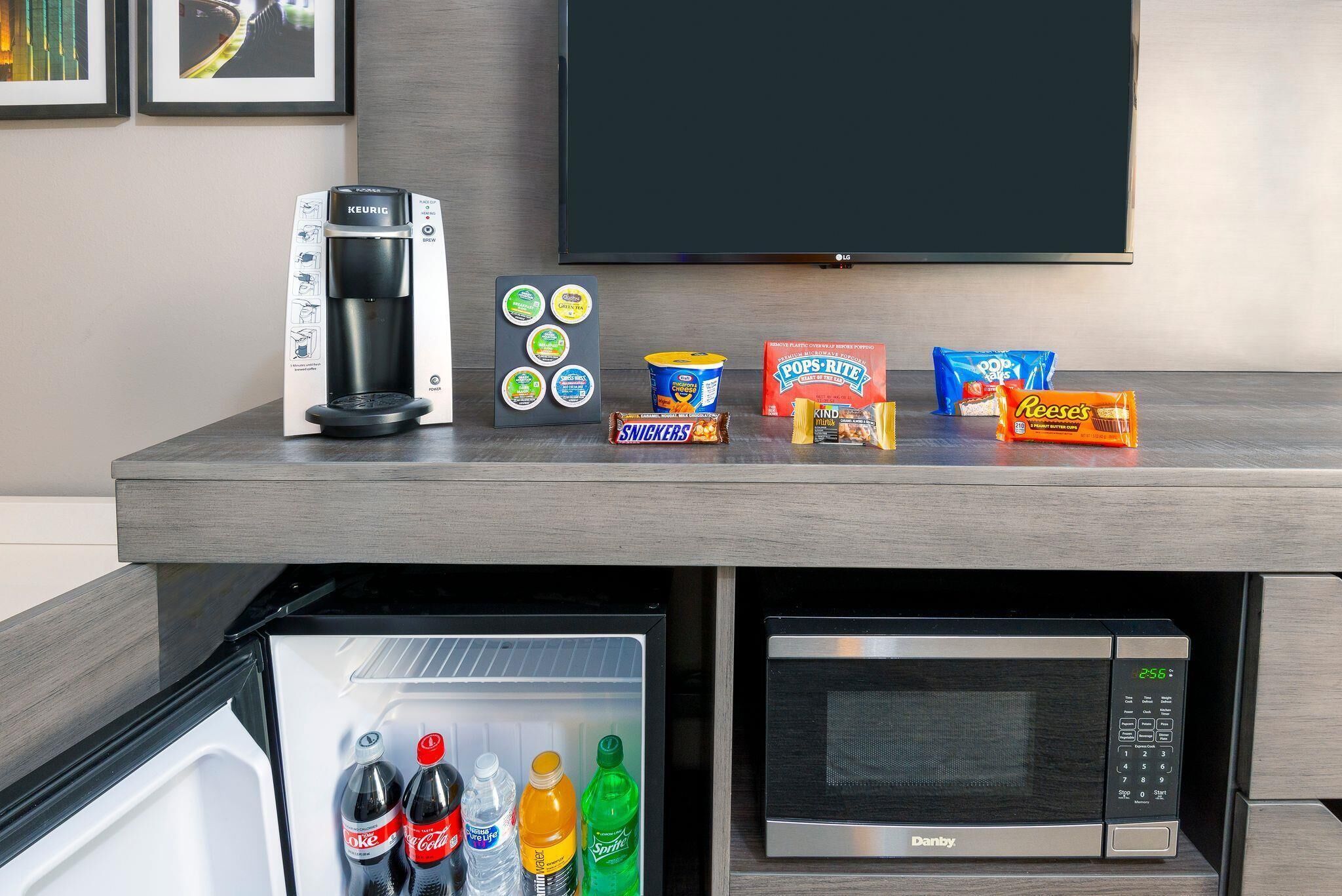 Una kitchenette con cafetera Keurig, microondas, refrigerador y diferentes opciones de bocadillos.