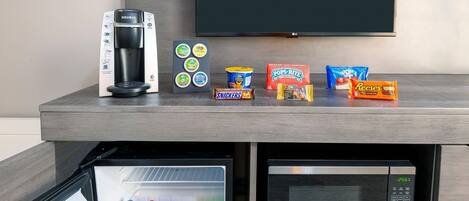 Una kitchenette con cafetera Keurig, microondas, refrigerador y diferentes opciones de bocadillos.