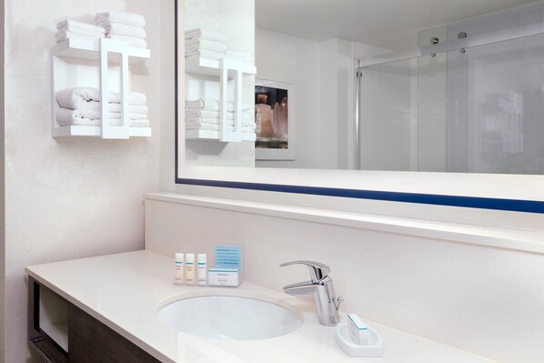 Un baño con un lavamanos blanco, un espejo y una cabina de ducha con mampara de vidrio.