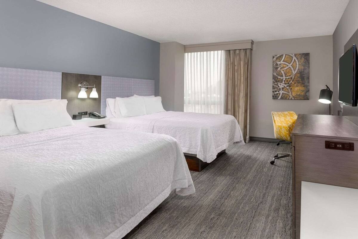 Une chambre d’hôtel avec deux lits, un bureau, une chaise, une télévision et une fenêtre avec des rideaux.